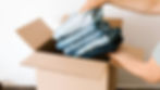 A man putting a bunch of clothes in a brown coloured box