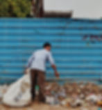 A man is picking up waste with a stick holding a white colour waste disposing bag