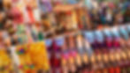 Vibrant New Delhi flee market scene with colorful fabrics, embroidered shoes, and handmade bags. Shoppers browse under a patterned canopy with lights.