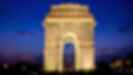 India Gate illuminated at night against a clear blue sky. Three flags are visible beneath the arch. The mood is serene and majestic.